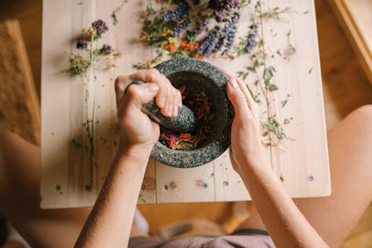 About Top view of hands grinding dried herbs and petals with a mortar and pestle on a wooden table.
